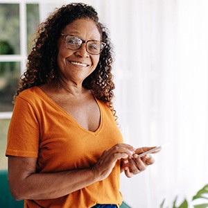 Senior woman with glasses smiling while looking at phone