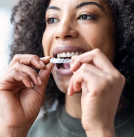 Smiling blonde woman holding an Invisalign clear aligner