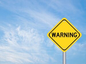 Yellow warning sign against blue sky background 
